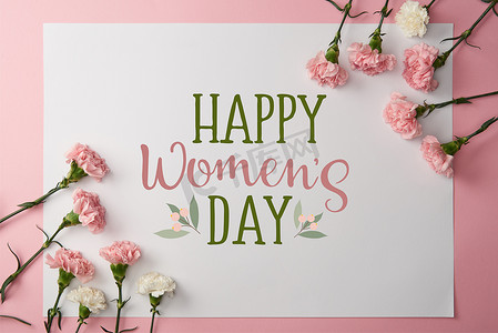 top view of pink and white carnation flowers and greeting card with happy womens day lettering on pink background