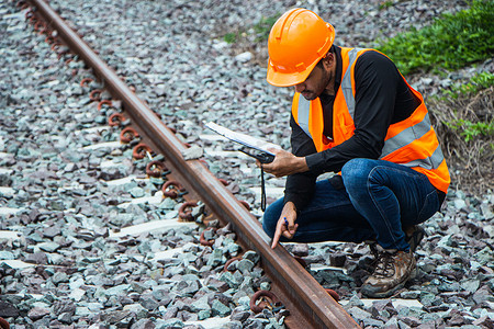 戴钢盔摄影照片_督察工程戴着钢盔和背心,检查铁路轨道上的铁路建设工作.亚洲工人和同事站在旧火车车厢旁边.