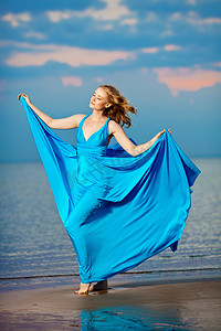 在海滩上的长长的蓝色晚礼服的豪华女人。美 