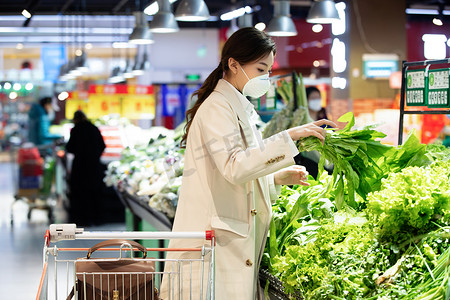 健康安全食品摄影照片_戴口罩的青年女人在超市购买青菜