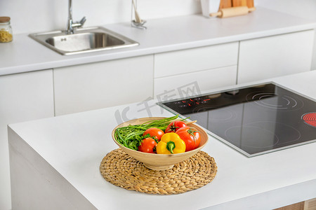 蔬菜在烹调加热器和背景上的接收器的感应与现代白色厨房里的碗的特写