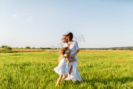 在刮风的日子里, 母女俩在绿色的草地上一起玩耍, 拥抱着。