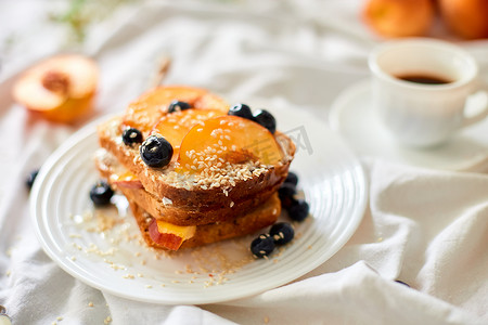 cheese摄影照片_Breakfast on white bed sheets, good morning, summer french toast with cream cheese, honey, peaches and blueberries, coffee, flowers, Hotel room early morning, honeymoon