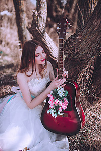 美丽浪漫的欧洲姑娘，带着带着鲜花的吉他，在户外摆姿势。音乐与自然的概念。春天的时间.