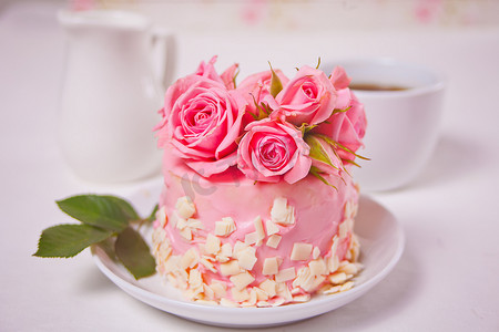 有粉色釉料的小蛋糕，漂亮的玫瑰，一杯咖啡，白桌子上的礼品盒