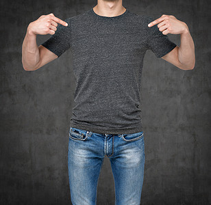 Close-up of a man pointing his fingers on a blank grey t-shirt. Dark concrete background.