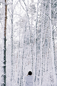 在白雪皑皑的森林里行走的女孩的后视图