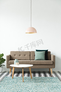 沙发的前视图与枕头, 茶几, 吊灯和绿色地毯设置在客厅内的白色墙上