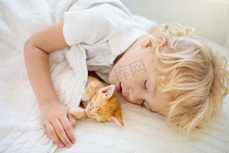 男婴和小猫睡在白色针织毛毯上.孩子和猫。孩子和宠物。带着他的动物的小孩温暖的冬夜和宠物在一起.孩子们和动物玩耍。小猫咪和小猫咪的睡眠.