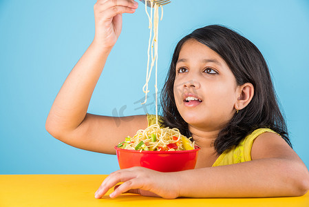 快乐的亚洲孩子吃美味的面条，小印度女孩吃面条在红碗，在蓝色的背景