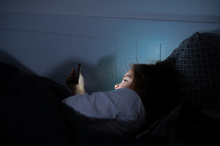 小女孩晚上睡觉前在床上看智能手机上的视频