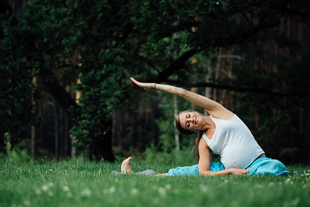 实心瑜伽柱摄影照片_在荷花的立场上森林背景的孕妇瑜伽。在公园草地垫、 户外、 健康女人.