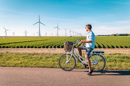 年轻男子电动绿色自行车被风车农场隔离，风车在美丽明亮的一天被荷兰弗洛尔和诺德鲁斯特沃尔德隔离