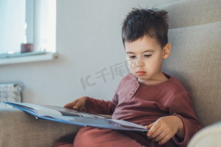 上学的摄影照片_一个小男孩坐在沙发上学习一个人在家专心看书的画像。阅读，认知能力。教育、学习、学习.