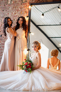婚礼照片摄影照片_美丽的金发新娘在豪华婚纱和漂亮的双胞胎伴娘在一个早晨在阁楼空间与镜子和花环灯。时尚现代婚礼照片.