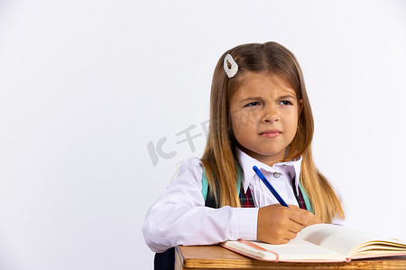 穿着校服、穿着紧身衣的小女孩孤零零地坐在书桌前，白色背景。女学生不喜欢做作业. 