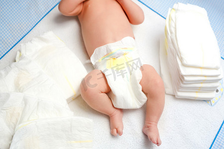 干性摄影照片_用尿布把新生婴儿的脚放在更衣室的桌子上。可爱的小女孩或男孩两个星期大。干性和健康的身体和皮肤概念。幼儿保育.