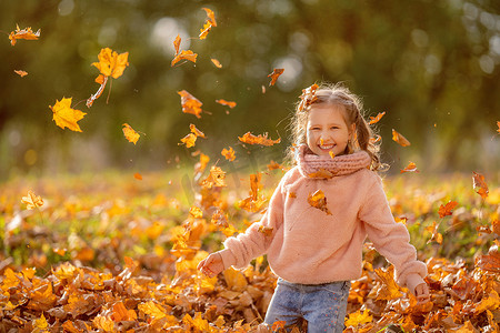 在一个阳光灿烂的日子里，快乐的小女孩在秋天的公园里抛撒着秋天的树叶，在外面笑着。孩子对秋天的到来感到高兴，玩着五彩缤纷的树叶.