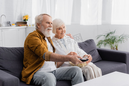 在沙发上看爆米花的老夫妇笑着看电视 
