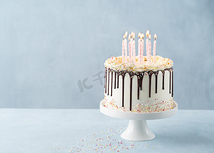 生日滴蛋糕上有很多粉红的蜡烛，上面有巧克力心绞痛，还喷涂在带有派对装饰的浅色背景横幅上。复制空间。庆祝的概念。潮流滴蛋糕。有选择的重点.