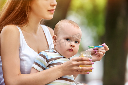 断奶摄影照片_婴儿喂养勺由母亲在户外公园。断奶 .