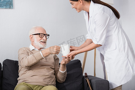 老年护士给坐在沙发上的老人倒杯茶