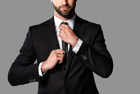 裁剪视图的时尚英俊商人在黑色西装固定领带隔离在灰色