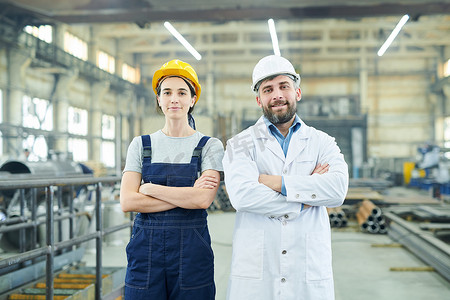 workshop摄影照片_Waist up portrait of two modern factory workers looking at camera while posing in industrial workshop