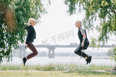 在公园与跳绳一起成熟的运动员和女运动员训练的侧视图