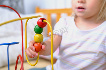 girl 3 years old plays with colored wooden educational labyrinth for kids, close-up of hands of cute child, development of fine motor skills, concept of development of creativity, interest in toys