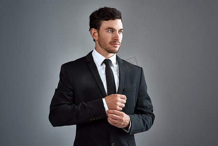 Dress with purpose. Studio shot of a handsome young businessman dressed in a suit against a grey background