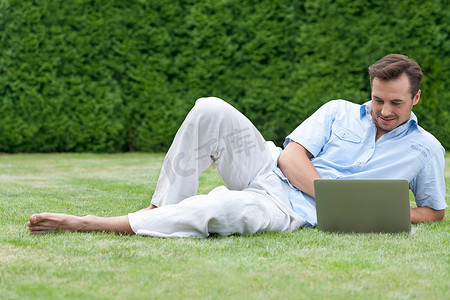躺在草地上同时使用笔记本电脑的人