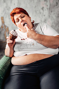 坐在扶手椅和吃甜蛋糕, 懒惰, 肥胖和不健康饮食概念的超重妇女
