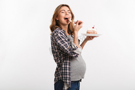 快乐的年轻怀孕的妇女吃蛋糕隔离白色