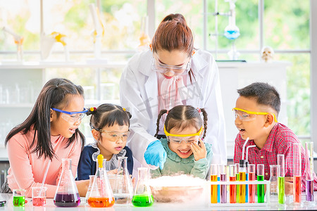 科学老师在实验室教亚洲学生, 烟从碗里飘出来, 他们兴奋, 五颜六色的试管和显微镜放在实验室的桌子上, 在实验室学习的概念.