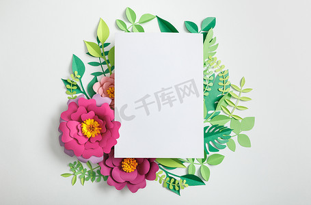 纸花上的白色空白卡片的顶视图和灰色背景上的绿叶