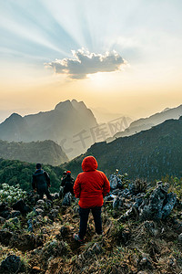 在泰国清迈清迈蒋刀道的背景下，冒险家们穿着红色的帽衫，在夕阳西下，带着高山和黄昏。从山顶拍张照片.