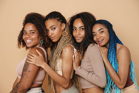 年轻的黑人4个女人在被米色背景隔离的相机前拥抱和微笑