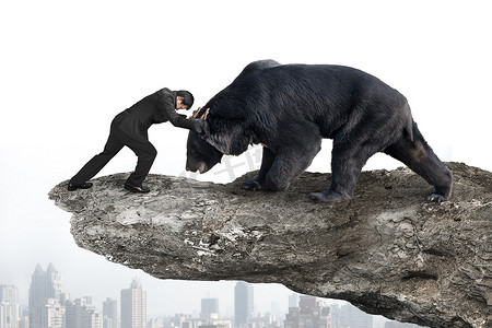 fighting摄影照片_Businessman fighting against black bear on cliff with sky citysc