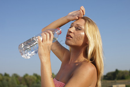 炎热摄影照片_年轻女人喝水，在炎热的夏天