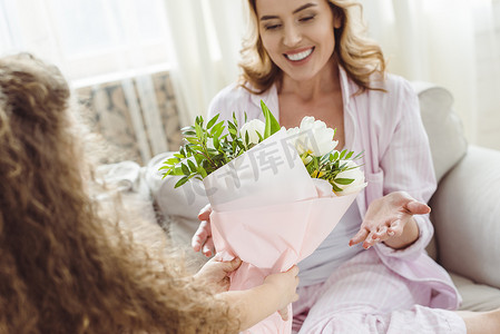 花束妈妈摄影照片_女儿在母亲节快乐的母亲面前献上花束给她微笑的妈妈。