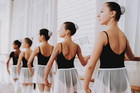 可爱芭蕾摄影照片_室内年轻女孩团体的芭蕾培训。古典芭蕾。巴莱丽娜·图图的女孩。室内训练。可爱的舞者大厅里的表演。舞蹈练习。穿白色衣服的女孩.