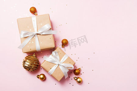 圣诞贺卡的组成。 纸制礼物，白色缎带，粉色背景，圣诞金球和五彩纸屑明星。 平平静静，顶视图，时尚风格.