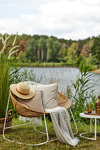 湖上的室外花园别致的构图，配有设计藤椅、咖啡桌、格子花、枕头、饮料和典雅的配饰。夏天的寒意.