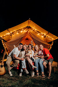 夏天的夜晚，在舒适的篝火边，一群快乐的威尔士科吉彭布罗克犬的朋友们放松地在人群中打滚。豪华野营帐篷，用于户外娱乐和娱乐。生活方式概念