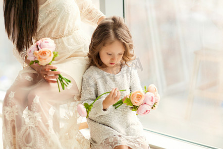 妈妈和女儿站在一个巨大的窗户旁边, 女儿在母亲节那天给妈妈送花。.
