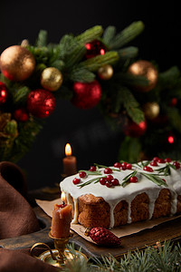 圣诞摄影照片_传统圣诞蛋糕的精选焦点，在圣诞花圈附近放上覆盆子，在木制桌子上点燃蜡烛，与黑色隔离