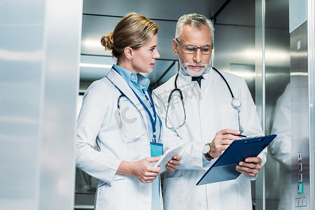 成熟男性医生显示剪贴板的女性同事与数字片在医院电梯 