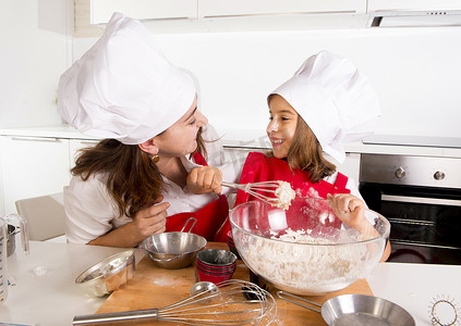 happy购摄影照片_happy mother baking with little daughter in apron and cook hat with flour dough at kitchen