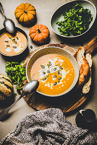 秋天，冬季暖化季节餐。 平面南瓜汤与种子，欧芹和奶油在灰色混凝土背景的碗，顶部视图。 素食、健康、舒适食物的概念